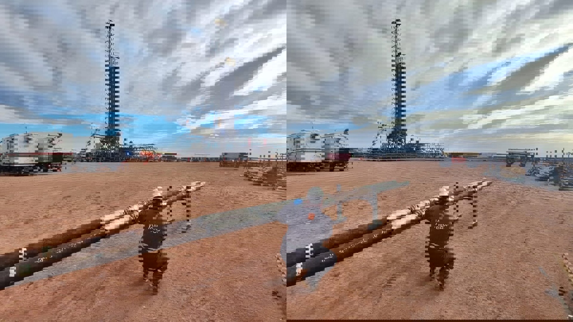 Welltec engineer kneeling and inspecting completion tools on the rig floor, with drilling equipment and a clear sky in the background.