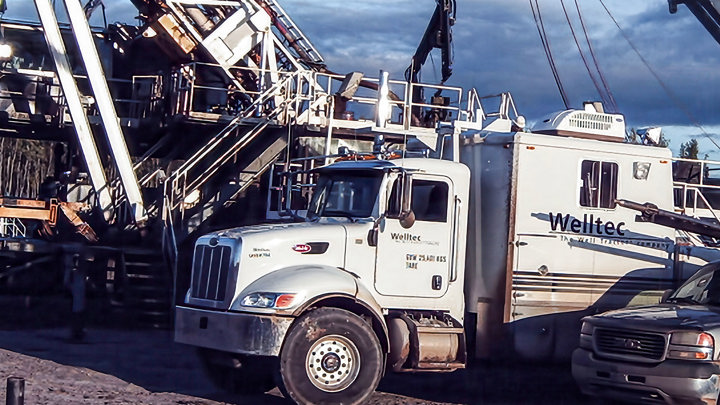 Welltec E-line intervention truck at a shale oil wellsite, supporting efficient well intervention operations with rig equipment in the background.