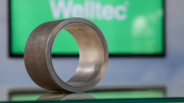 Isealate component by Welltec displayed with a blurred Welltec logo in the background, showing a circular metallic part.