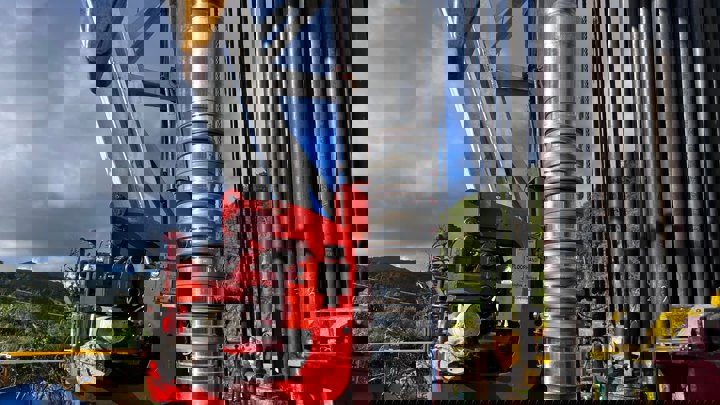 A drilling rig with a prominent large pipe atop it, showcasing industrial equipment against a bright sky.