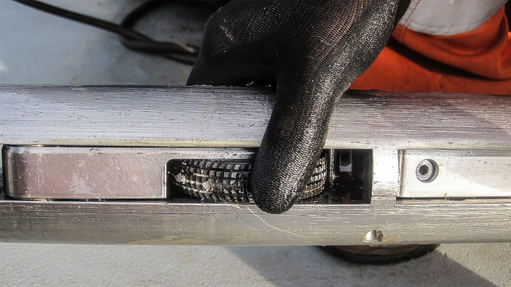 Close-up of a Welltec tool with a gloved hand holding a scale cleanout device, exposing the cleaning element designed to improve perforation access.