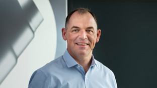 Kevin Wood, WCS Sales Director for the Middle East, standing in front of a dark background wearing a blue shirt and smiling.