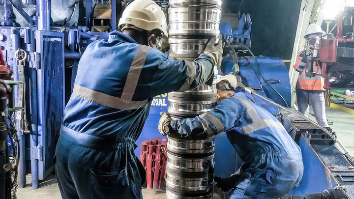 Two offshore engineers actively working on a large pipe related to high temperature 812WAB for well-relining.