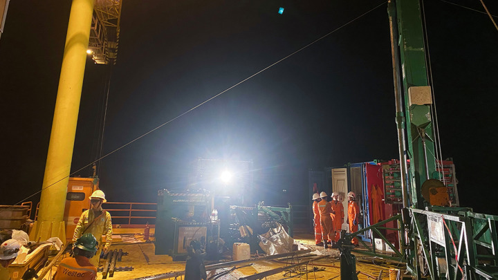 Engineers working on an oil platform at night under bright lights during equipment operations.