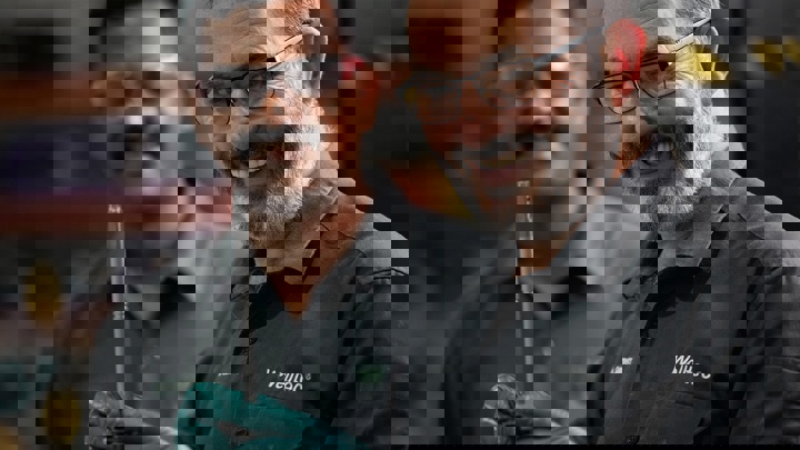 Welltec engineers smiling while holding a precision tool in the workshop, with one engineer in the background wearing safety glasses.